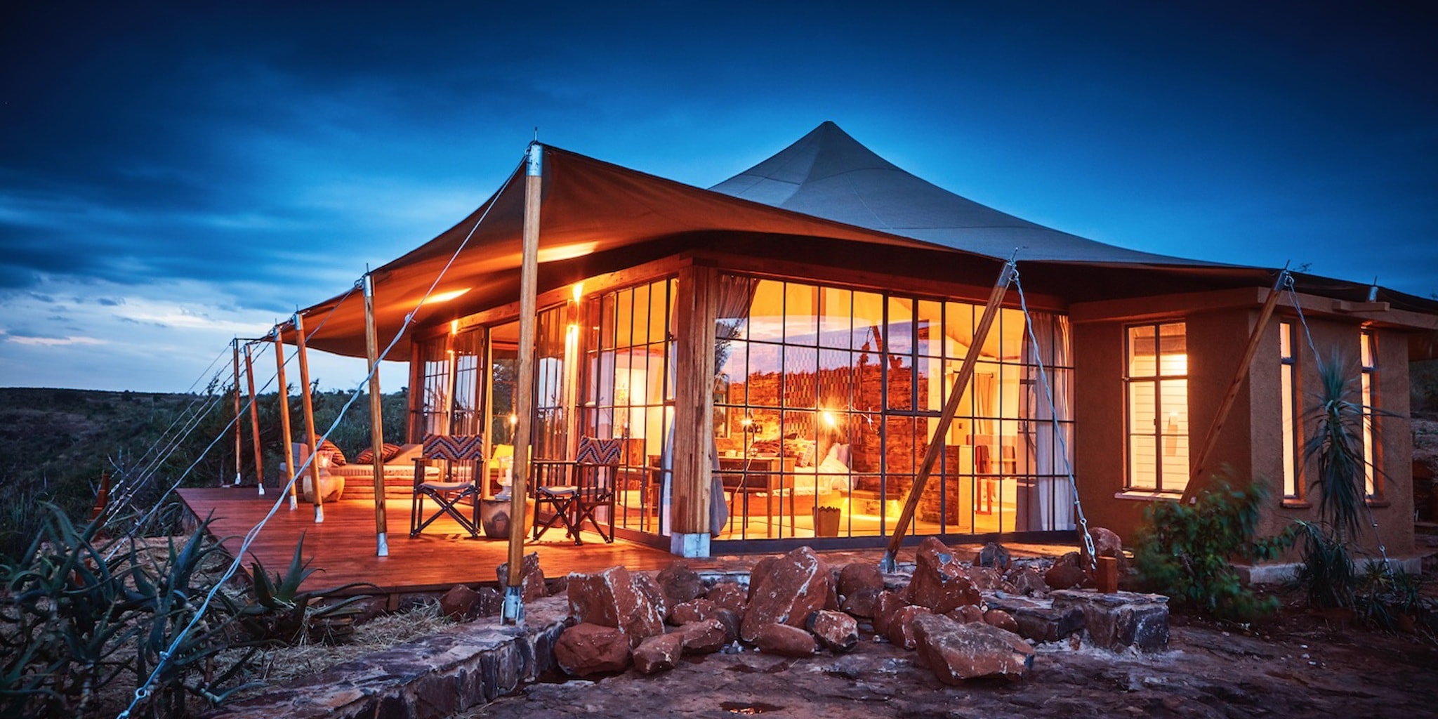 A luxurious safari camp featuring spacious tents overlooks the vast African savanna, bathed in the warm hues of sunset. This picturesque scene captures the essence of Kenya tours, inviting guests to experience the stunning landscapes and wildlife of the Maasai Mara National Reserve.