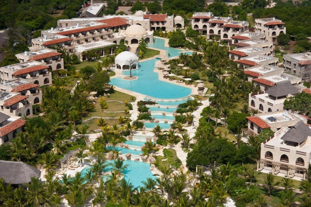 An aerial view of Swahili Beach Resort in Diani shows cascading turquoise pools winding through lush palm trees, surrounding several pools creating a serene, luxurious coastal oasis