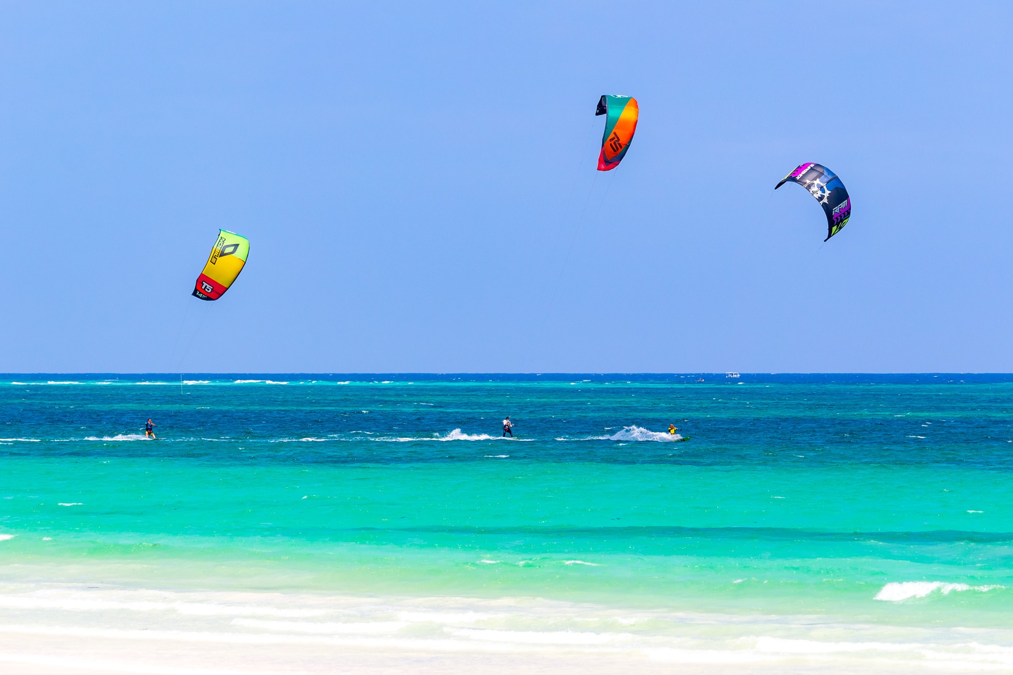 Colorful kitesurfers riding turquoise waves at Diani Beach, Kenya.