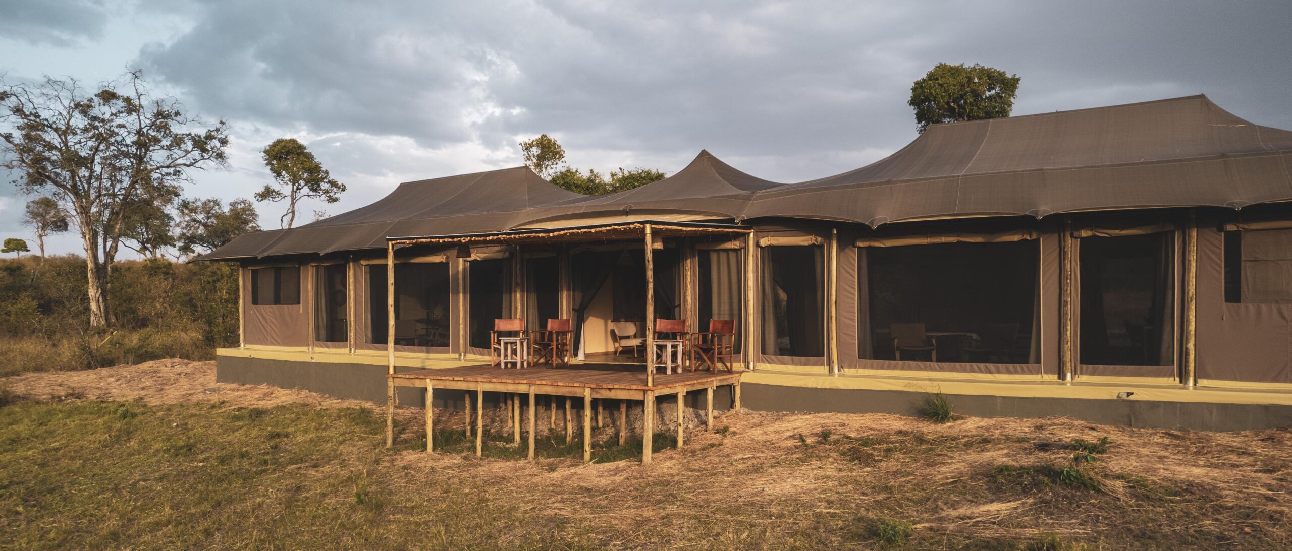 Entim Private Luxury Camp tented suite with wide verandah, safari chairs, and canvas walls set on a raised deck overlooking Masai Mara under a dramatic evening sky.