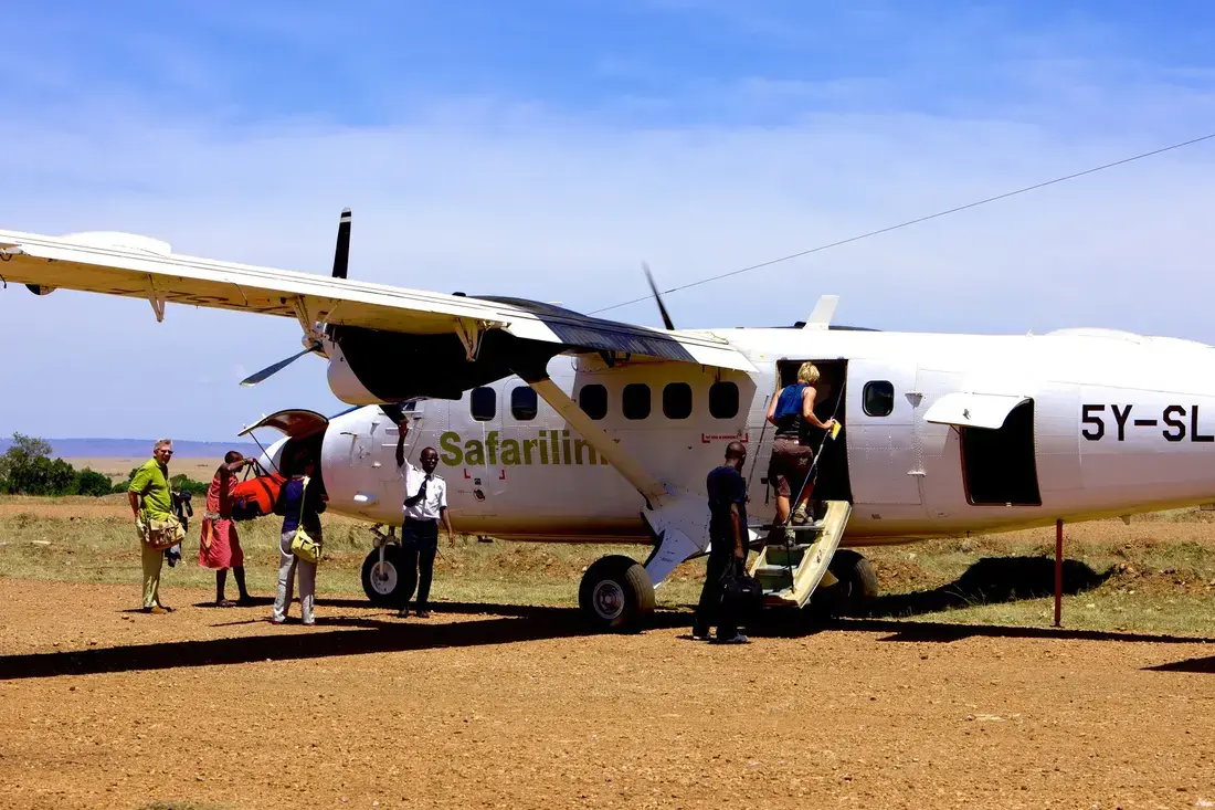 Guests boarding a light aircraft on an Airstrip in Masai Mara airstrip, with staff assisting and luggage being loaded under a clear blue African sky.