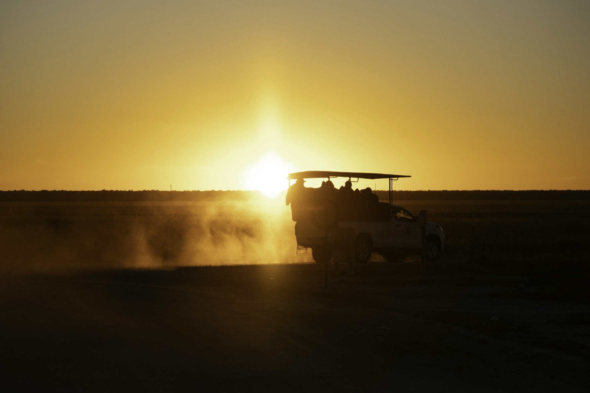 A safari vehicle driving through the Masai Mara at sunset.